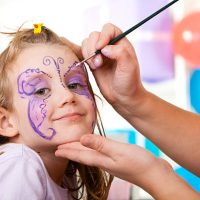 Little smiling girl having face painted on birthday party.